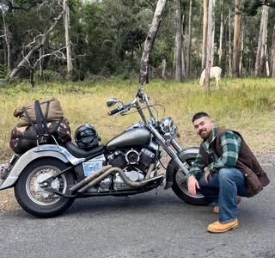 Reilly crouched beside his motorcycle on a bush road